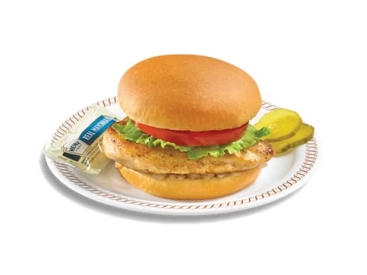 A grilled chicken sandwich with tomato and lettuce on a white plate.