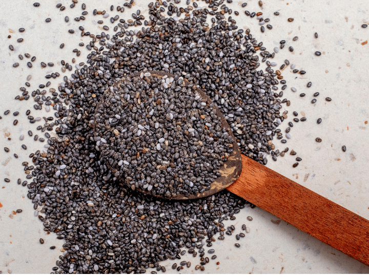 A spoon of chia seeds with a bunch of seeds around it.