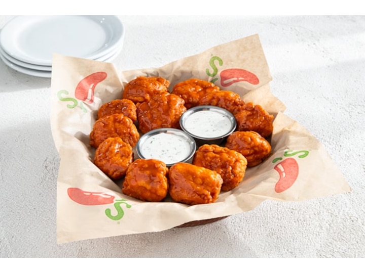 A bunch of boneless buffalo wings with two cups of ranch in a basket.