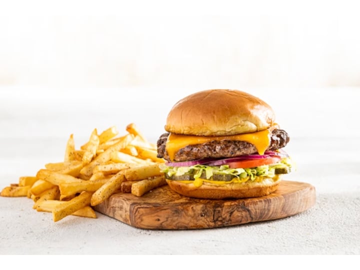 A black bean burger with cheese, lettuce, tomato, and onion on a wood cutting board with fries.