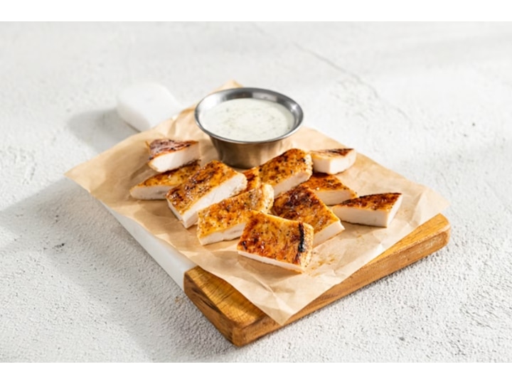 A bunch of grilled chicken on parchment paper on a wood cutting board.