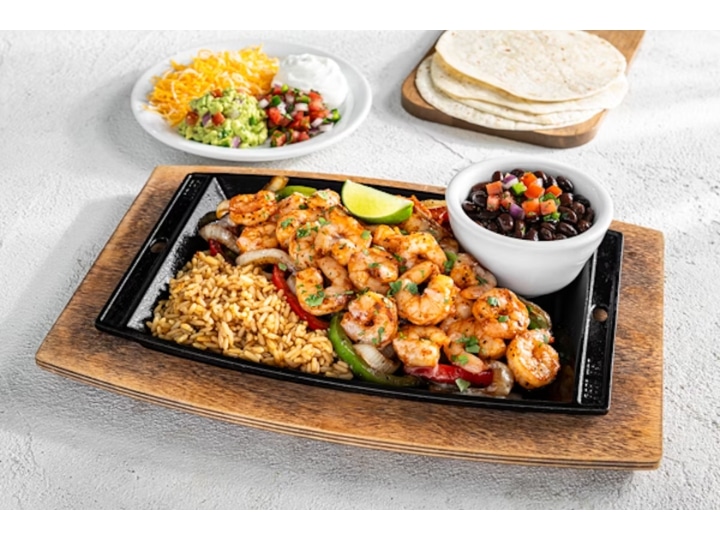 A bunch of grilled shrimp, rice, fajita veggies, and black beans on a plate.