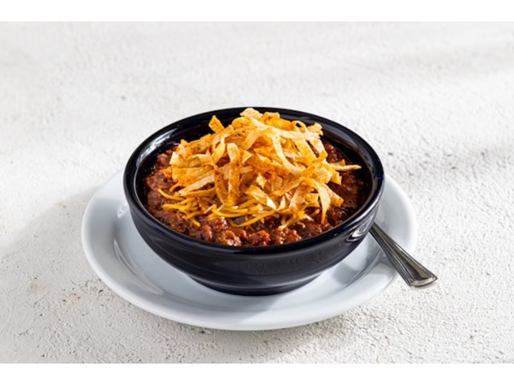 tortilla strips on top of cheddar cheese on chili in a black bowl.