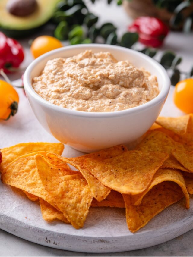 A bowl of low calorie queso dip on a wooden serving board with tortilla chips.