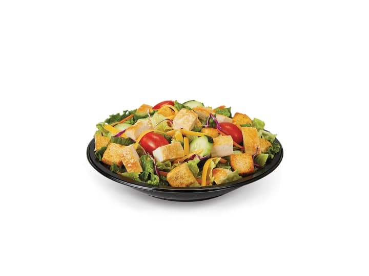 A mixed greens salad with grilled chicken pieces, croutons, tomato.