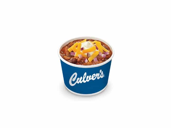 A cup of chili with shredded cheese and sour cream on top.