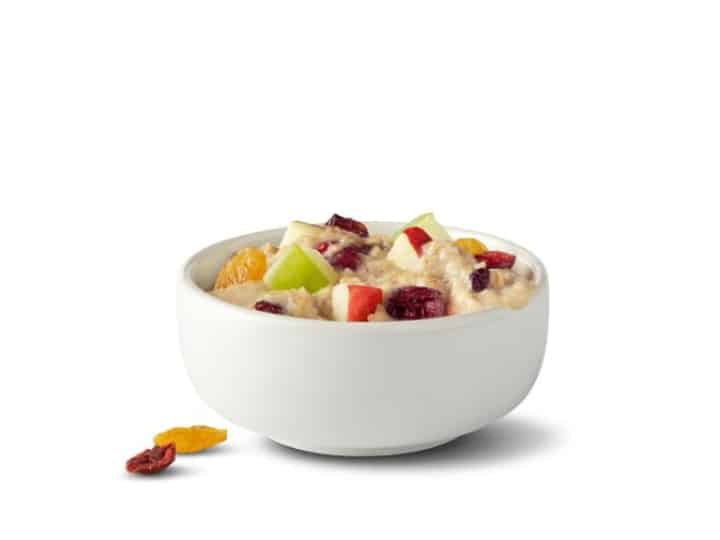 A bowl of oatmeal with sliced apples and dried cranberries on top