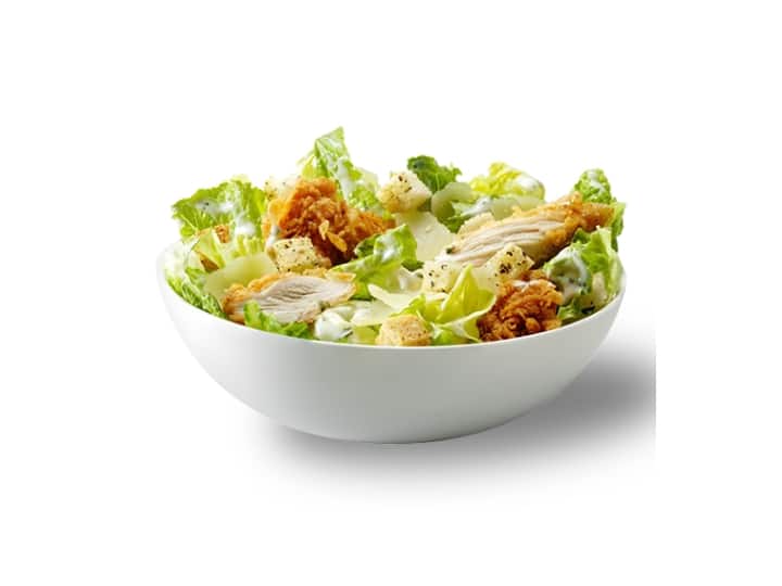 A white bowl filled with lettuce, fried chicken, and caesar dressing.