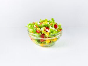A glass bowl filled with lettuce, corn, and tomatoes.