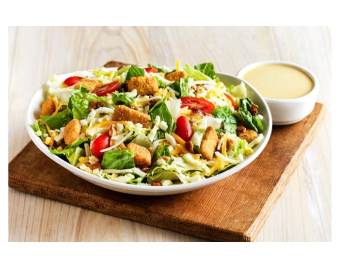 A cobb salad in a white bowl on a wood cutting board with ranch.