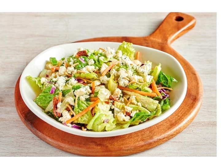 A salad with blue cheese crumbles and chopped pecans in a white bowl.