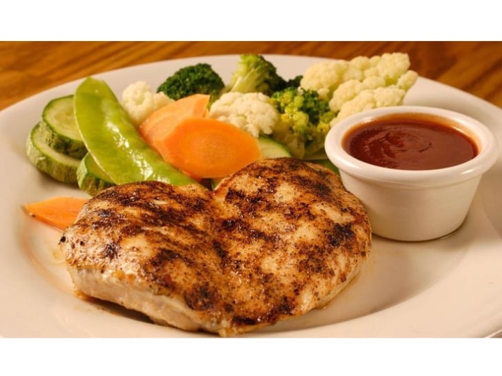 Two seared chicken breasts with veggies on a plate.