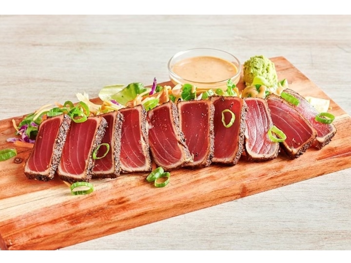 A bunch of sliced ahi tun on a wooden cutting board.