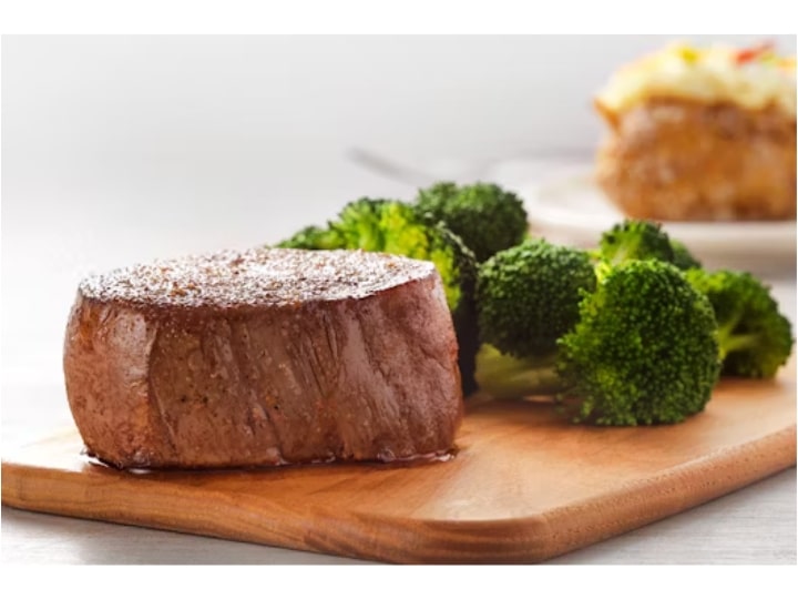 A large piece of filet mignon on a wood board with broccoli.