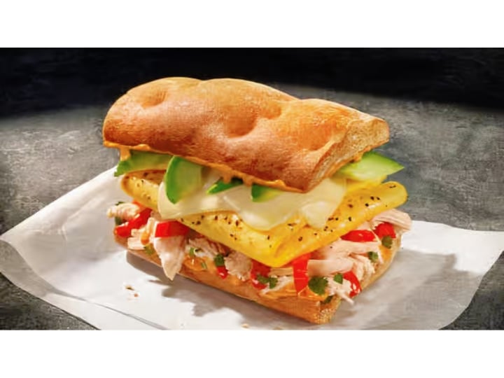 A sandwich with egg, chicken, avocado, peppers, and cheese on a cibatta roll.