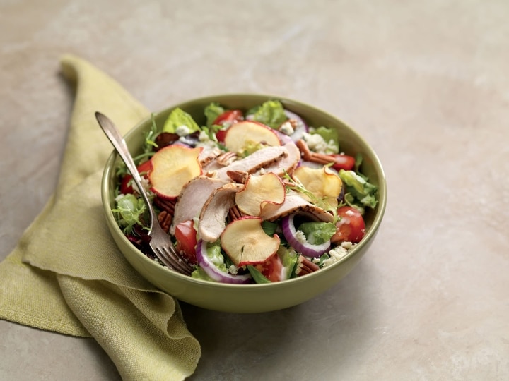 A bowl of salad with apple chips, chicken, onion, tomato, and cucumber.