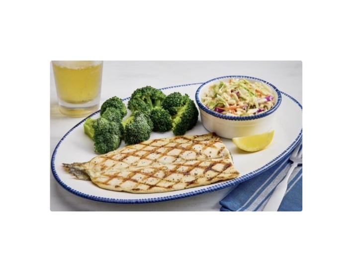 A grilled rainbow trout on a plate with broccoli and coleslaw.