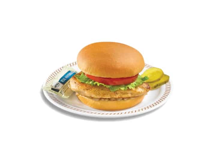 A grilled chicken sandwich with lettuce and tomato on a white plate.