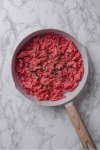 An overhead shot of a ceramic skillet with raw ground beef cooking in it.