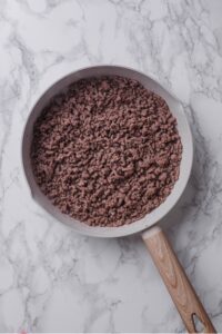 An overhead shot of a ceramic skillet with cooked ground beef.