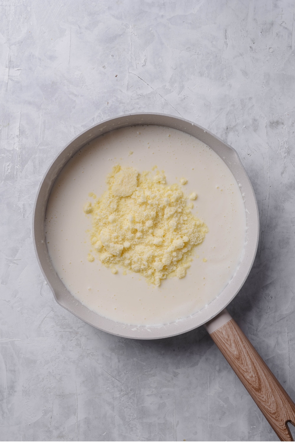 An overhead shot of a ceramic skillet filled with a low calorie alfredo sauce mixture, with grated parmesan chese piled on top.