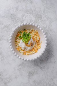 An overhead shot of a white porcelain bowl filled with grated hard boiled egg, greek yogurt, mustard, and chopped green onion.