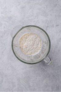 An overhead shot of a glass blender filled with milk, flour, and cream cheese.