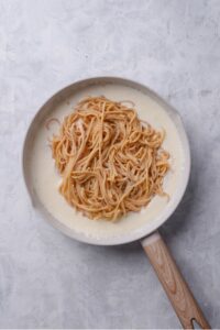 An overhead shot of a ceramic skillet filled with low calorie alfredo sauce, with cooked spaghetti on top.