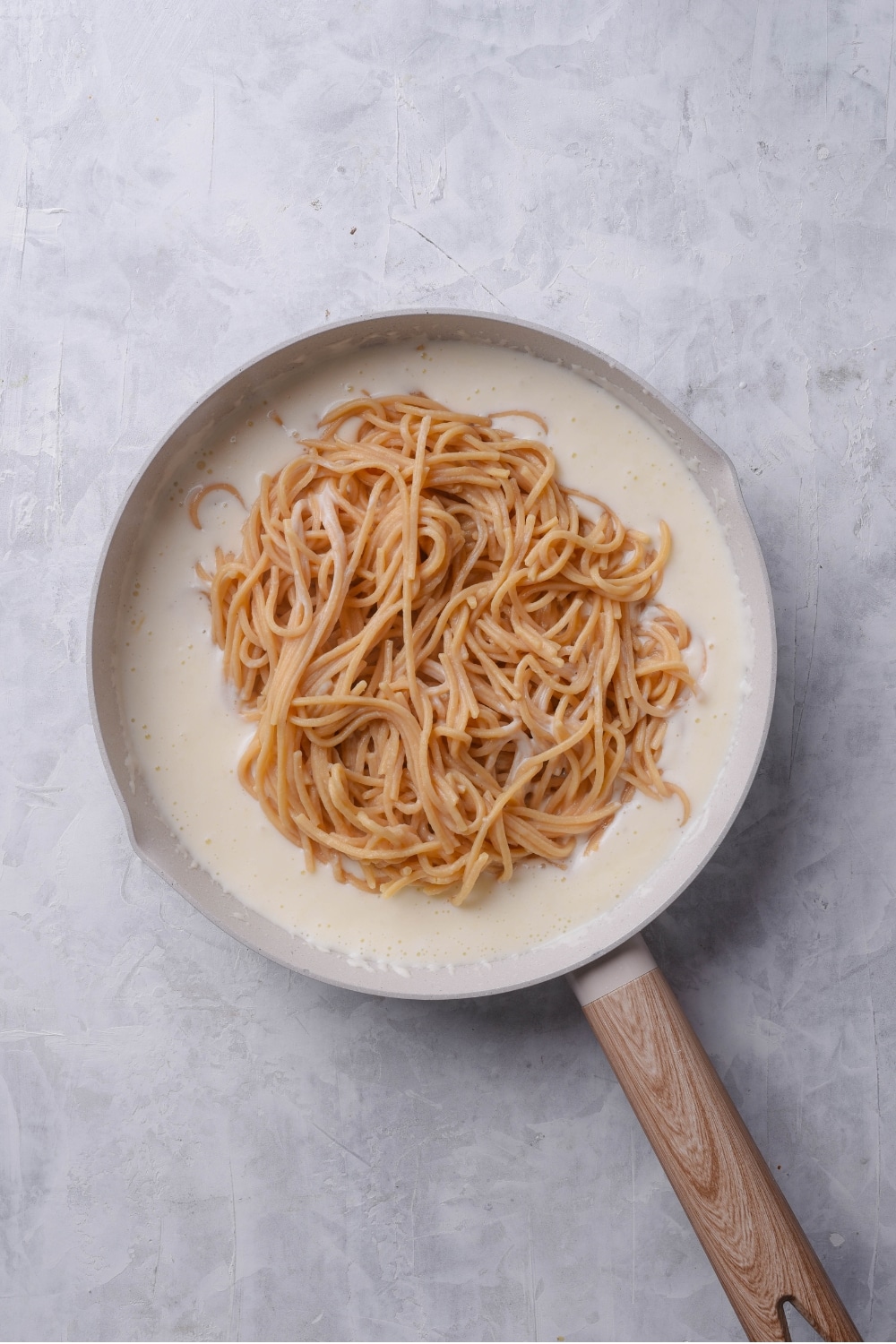 An overhead shot of a ceramic skillet filled with low calorie alfredo sauce, with cooked spaghetti on top.