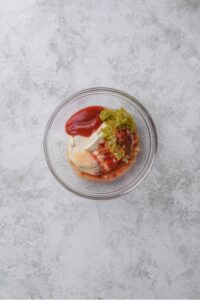 An overhead shot of a small glass bowl filled with ingredients for a low calorie big mac sauce mixture.