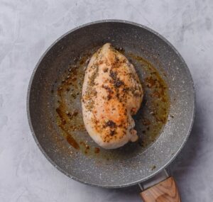An overhead shot of a ceramic skillet with cooked chicken breast.