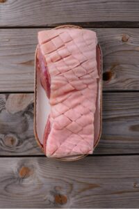 An overhead shot of pork belly with scored skin on a plate.