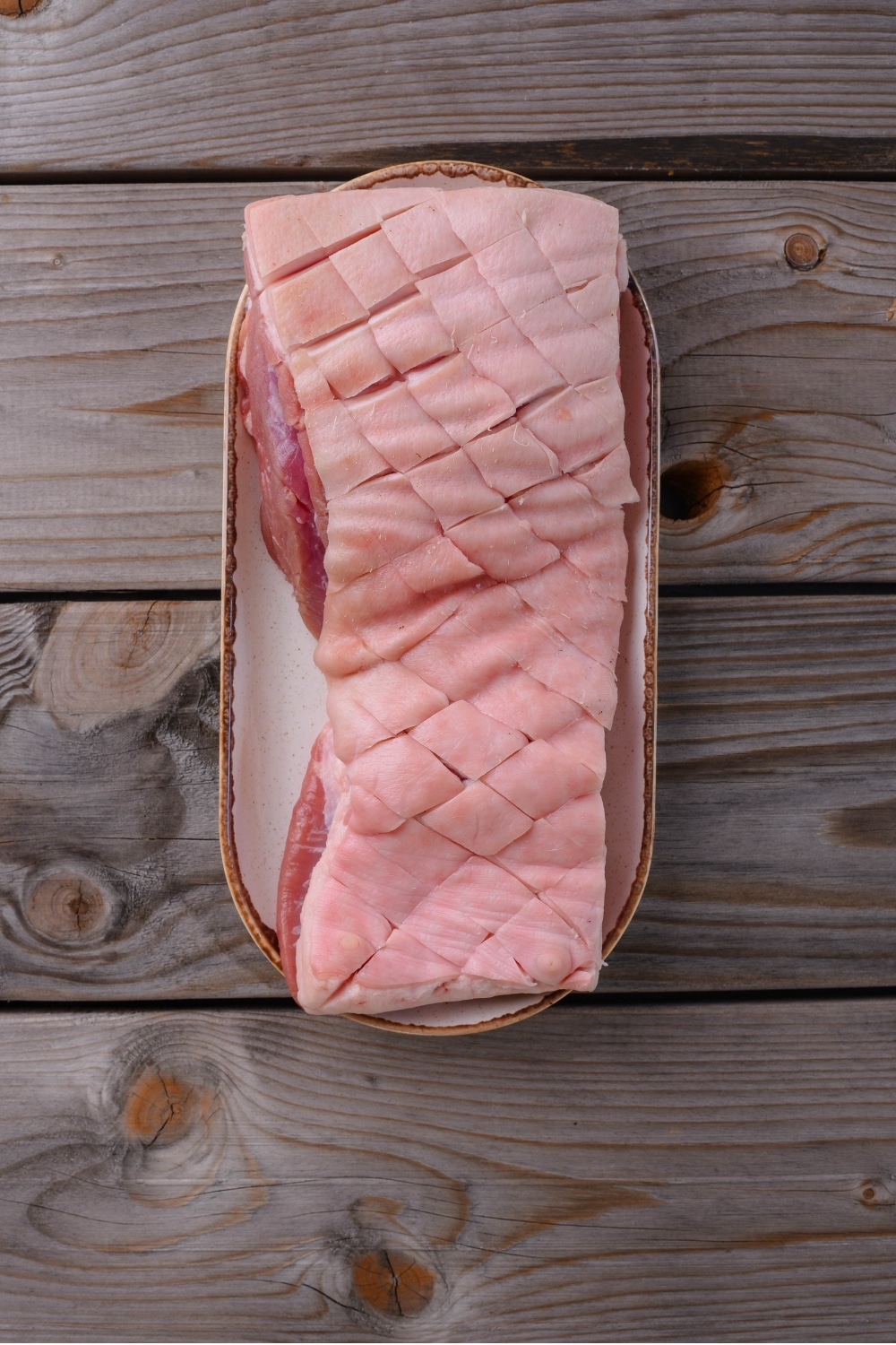 An overhead shot of pork belly with scored skin on a plate.