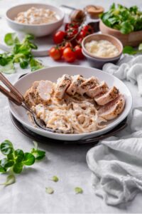 A ceramic plate filled with linguine in low calorie alfredo sauce, topped with sliced grilled chicken. There are two forks dipped into the pasta.