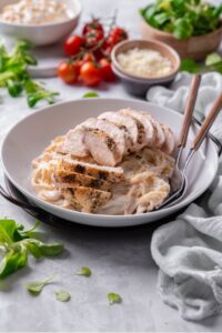 A ceramic plate filled with linguine in low calorie alfredo sauce, topped with sliced grilled chicken. There are two forks dipped into the pasta.
