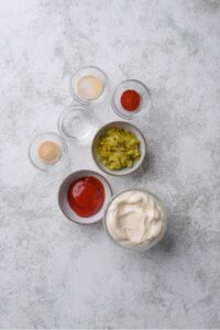 An overhead shot of several bowls filled with various ingredients for low calorie big mac sauce including mayo, ketchup, relish, vinegar, and spices.