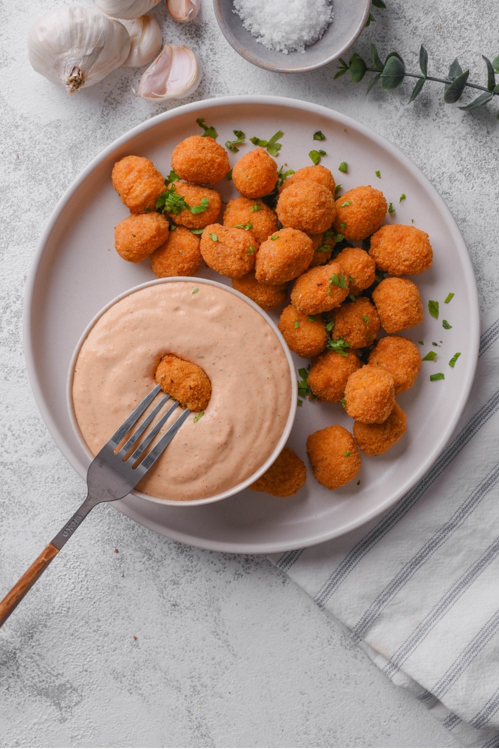 An overhead shot of a small ceramic bowl filled with low calorie big mac sauce served on a plate with popcorn chicken. There is a fork dipping a piece of chicken into the sauce.