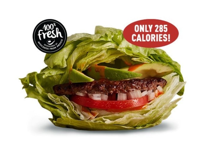 A burger in a lettuce wrap with tomato and onion.