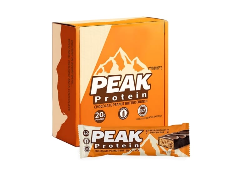 A PEAK protein bar inside of its packaging next to a box of bars.