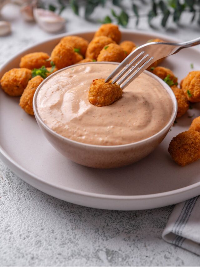 A small ceramic bowl filled with low calorie big mac sauce served on a plate with popcorn chicken. There is a fork dipping a piece of chicken into the sauce.
