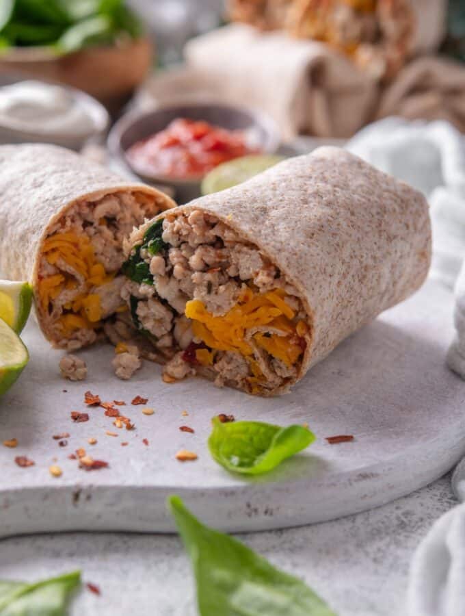 A burrito cut in half on a cutting board stuffed with ground meat, spinach, and cheese.