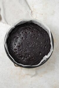 A circular cake pan lined with parchment paper filled with a freshly baked chocolate cake.