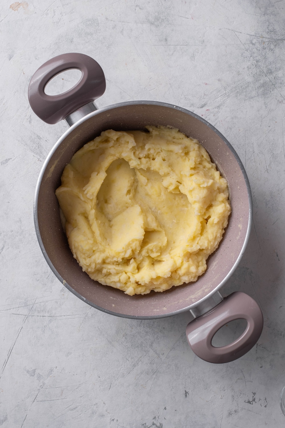 An overhead shot of a stock pot filled with mashed potatoes on a marble counter.