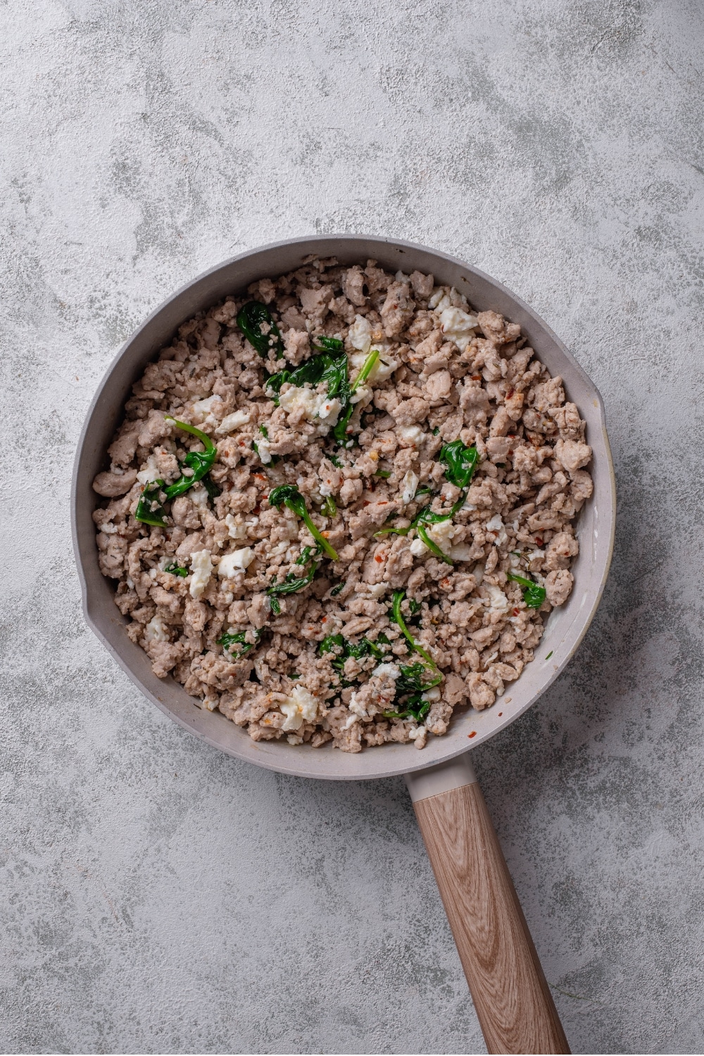 An overhead shot of a ceramic skillet with cooked ground turkey, egg whites, and spinach on a marble countertop.