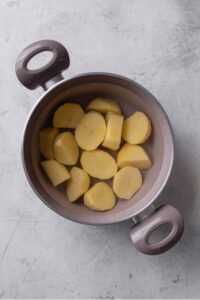 An overhead shot of a stock pot filled with water and cubed potatoes on a marble counter.