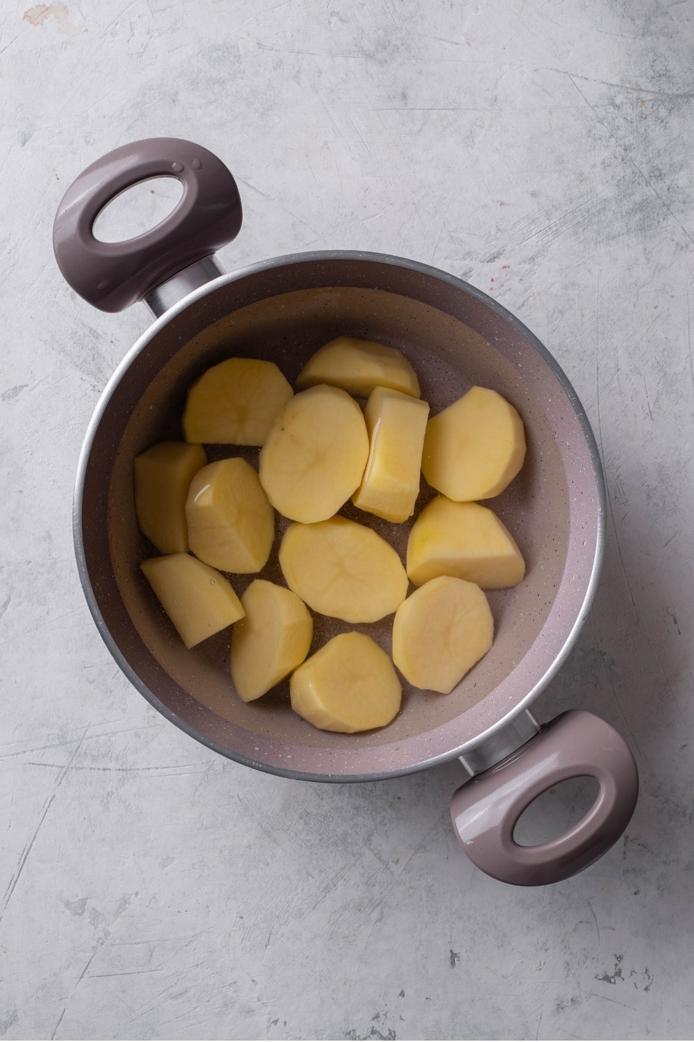 An overhead shot of a stock pot filled with water and cubed potatoes on a marble counter.