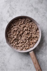 An overhead shot of a ceramic skillet with cooked ground turkey on a marble countertop.