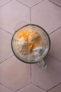 A blender filled with shredded cheese, cottage cheese, and seasonings.