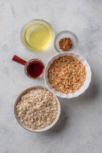 Overhead view of an assortment of ingredients including bowls of egg whites, rolled oats, maple syrup, cinnamon, and brown rice cereal.