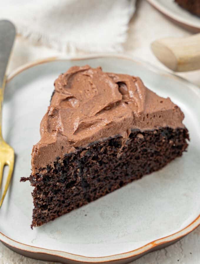 A slice of chocolate cake topped with chocolate frosting on a plate with a fork.